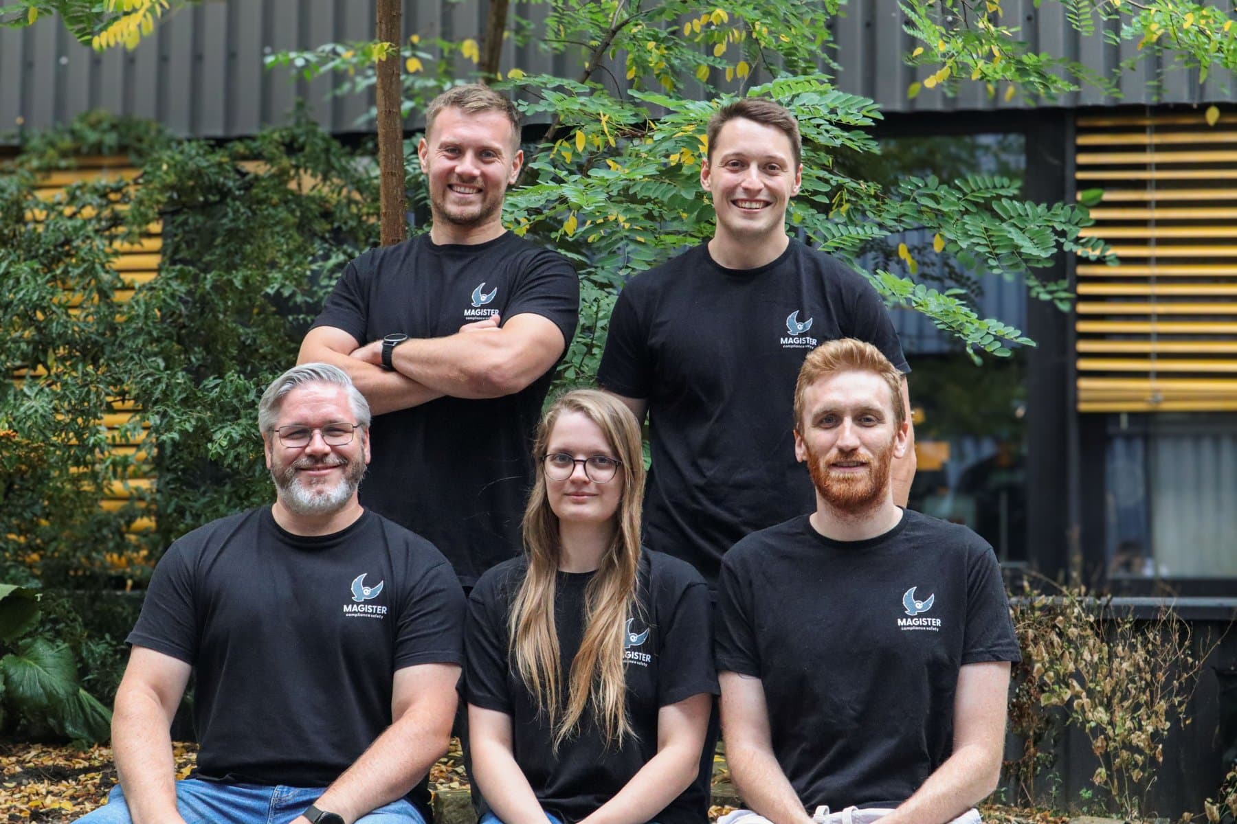 Das fünfköpfige Magister-Team in schwarzen Magister-T-Shirts vor einer begrünten Fassade